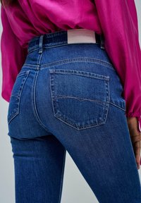 Džínové kalhoty v tmavě modré barvě s hladkou texturou. Obsahují dvě zadní kapsy s prošitým detailem a koženou nášivku s nápisem "Salsa Jeans."