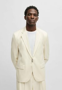 Light cream suit jacket with notched lapels, two front pockets, and a single-button closure. Smooth fabric with a tailored fit.