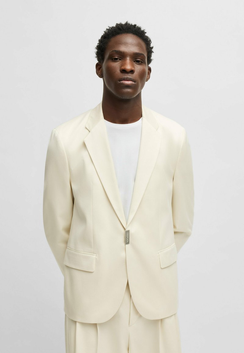 Light cream suit jacket with notched lapels, two front pockets, and a single-button closure. Smooth fabric with a tailored fit.