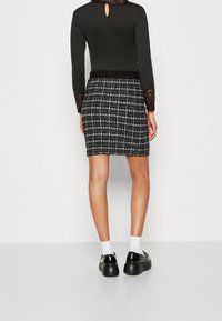Černý dlouhý rukáv top s krajkovými detaily, doplněný sukní do kolen s texturou v černobílé kostce. Černé platformové boty s bílými ponožkami.