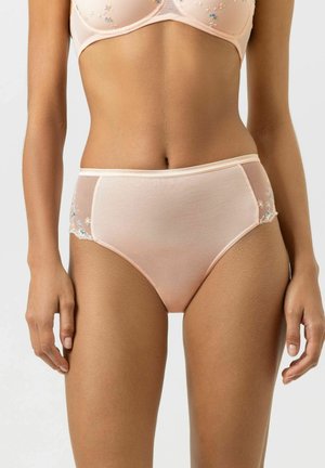 Vrouw draagt perzikkleurige high-waist slip met bloemrijke borduurwerk en bijpassende beha, staand tegen een effen lichte achtergrond.