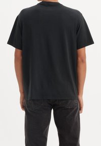 Czarny bawełniany T-shirt, krótki rękaw, okrągły dekolt, luźny krój. Bezszwowe plecy o gładkiej fakturze, w komplecie z ciemnymi dżinsami.