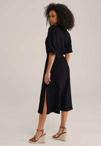 Svart midi-klänning med korta puffärmar, texturerad tyg, åtsittande midja och sprund på sidorna; matchad med bruna kilklacksandaler.