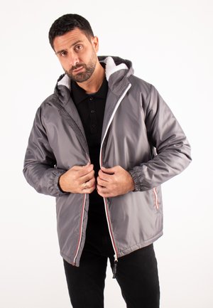 Veste grise zippée avec des poignets élastiques, une capuche doublée en polaire blanche et des accents rouges contrastants. Matière douce et lisse.