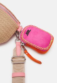 Sac tissé beige avec des accents roses, doté d'une fermeture éclair et d'une pochette colorée attachée en rose et orange avec des coutures décoratives.