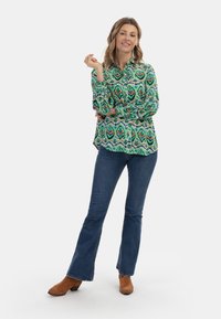 Camicia a maniche lunghe con motivo verde, design con bottoni, e jeans blu svasati. Indossata con stivaletti alla caviglia in camoscio marrone.