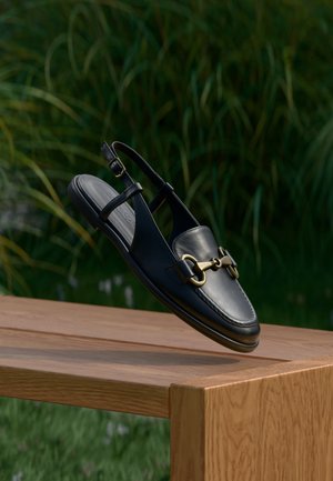 Schwarzer Slingback-Schuh aus Leder mit rundem Zehenbereich, goldfarbenen Akzenten und glatter Textur, präsentiert auf einer Holzfläche.