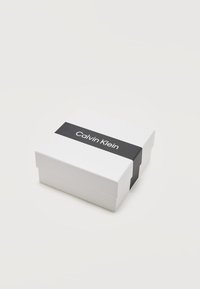 Λευκό ορθογώνιο κουτί Calvin Klein με μαύρη κορδέλα και το όνομα της μάρκας στην κορυφή, τοποθετημένο σε απλό φωτεινό φόντο.