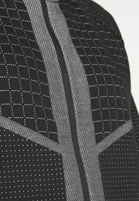 Černobílá vzorovaná látka s kombinací drobných čtverečků a teček, uprostřed se zipem, zobrazující různé textury a vizuální části.