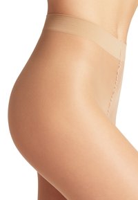 Calze beige con una texture liscia e una fascia elastica ampia. I dettagli delle cuciture sono visibili lungo il bordo. Il design è senza cuciture e aderente.