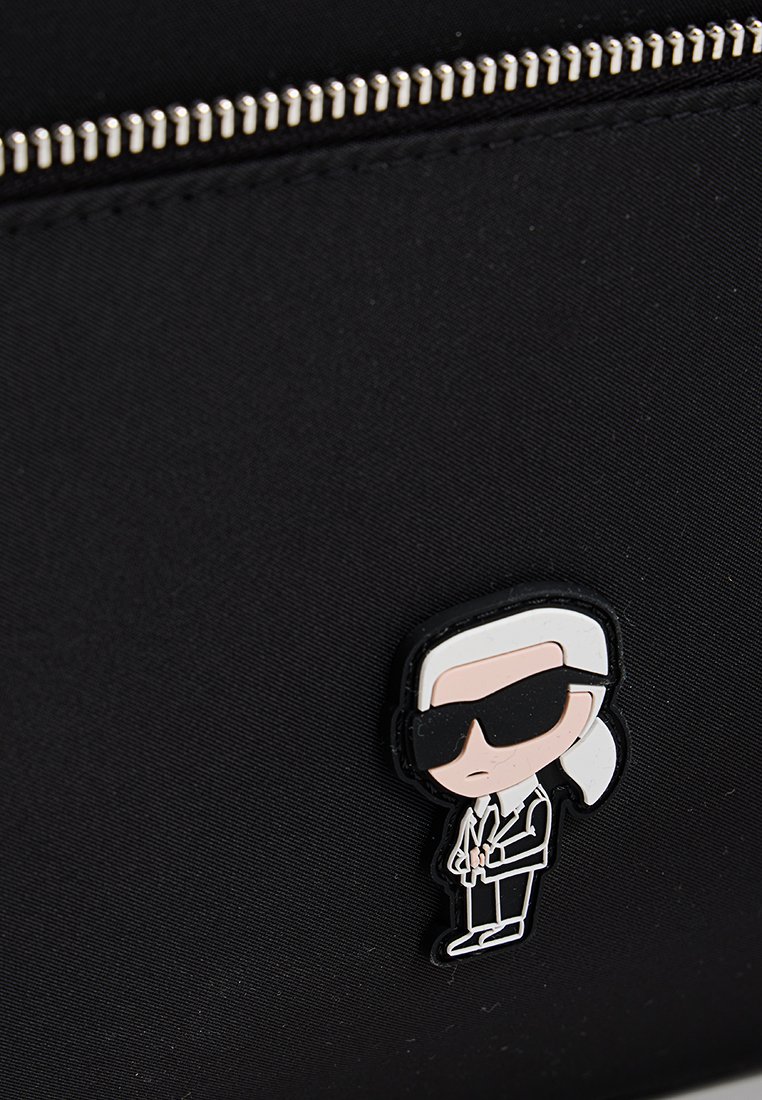 Bolsa de tela negra con un pin de personaje de dibujos animados con cabello blanco y gafas de sol, sosteniendo un par de tijeras, acentuando un diseño juguetón.
