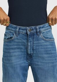Blå denimjeans med en klassisk femfickdesign, med en metallknap stängning och subtil blekning. Tyget har en texturerad yta.