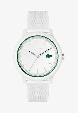 Orologio in silicone bianco con cinturino testurizzato, quadrante rotondo bianco, accenti verdi e logo Lacoste. Presenta indicatori e lancette delle ore minimalisti.