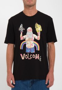 Sort bomulds t-shirt med et farverigt grafik af en skægget figur, der holder dyrehoveder, med "VOLCOM" tekst og regnbuebaggrund.