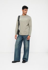 Cămașă gri cu mânecă lungă, cu logo embosat, combinată cu blugi albaștri cu picioare largi, cu detalii de cusătură. Geantă crossbody neagră și pantofi.