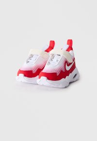 Par bijelih i crvenih dječjih tenisica s čičak trakama i povlačnim trakama, s Nike logotipom sa strane.