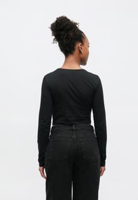 Svart langermet topp med rund hals, kombinert med svart høytlivs jeans med baklommer og teksturert finish.