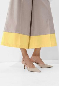 Tan slingback-hakken met puntneus en slanke hak, gecombineerd met een grijze rok met een brede gele zoom. Gladde textuur en minimaal ontwerp.