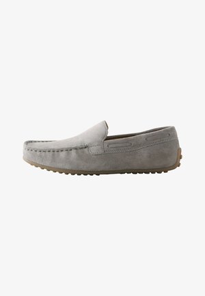 Mocasín de ante gris claro sin cordones con costura moc toe y suela de goma con clavos, visto de lado sobre fondo blanco.