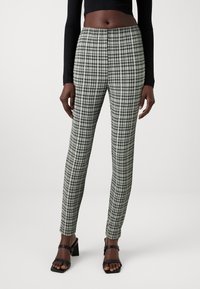 Hlače s uzorkom houndstooth u crno-bijeloj boji, uskog kroja, izrađene od teksturirane tkanine. U kombinaciji s crnim topom dugih rukava i cipelama na blok petu.