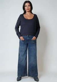 Marineblauw longsleeve shirt met een ronde halslijn en tekstdetails op de mouwen, gecombineerd met hoge taille wide-leg blauwe denim jeans.