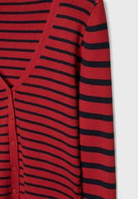 Cardigan rouge côtelé avec des rayures horizontales noires et des boutons sur le devant, montré de l'épaule jusqu'au milieu du torse sur un fond gris.