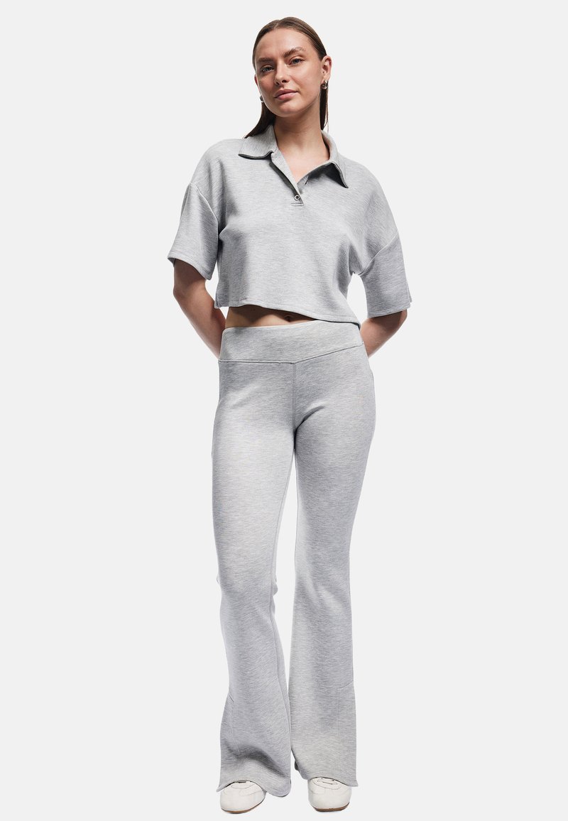 Graues Cropped-Top mit Kragen, kombiniert mit passenden, hochtaillierten, ausgestellten Hosen. Beide sind aus weichem, strukturiertem Stoff gefertigt. Weiße Sneakers runden das Outfit ab.