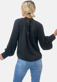 Svart blus med plisserade ärmar, rund halsringning och ett nyckelhål bak. Tillverkad av ett mjukt tyg med en ledig passform.