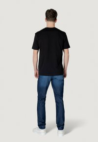 Camiseta negra de manga corta con cuello redondo, combinada con jeans azul oscuro y zapatillas blancas. Tela suave con un corte clásico.
