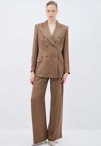 Abito marrone a doppio petto con colletto a contrasto, tessuto textured, pantaloni a gamba larga e due tasche frontali. Include bottoni rotondi.