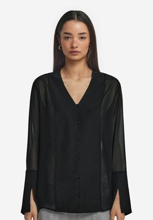 Blusa nera a maniche lunghe con tessuto trasparente, scollo a V, bottoni frontali e polsini spaccati. Vestibilità su misura con una texture morbida.