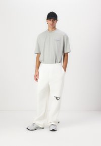 Grå bomulls t-skjorte med korte ermer og blå logo, kombinert med hvite joggebukser med et ørneprint og elastisk midjebånd. Hvite joggesko.