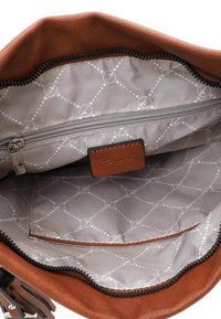Intérieur d'un sac à main en cuir brun, avec une doublure à motifs gris, un compartiment zippé et une poche ouverte pour l'organisation.