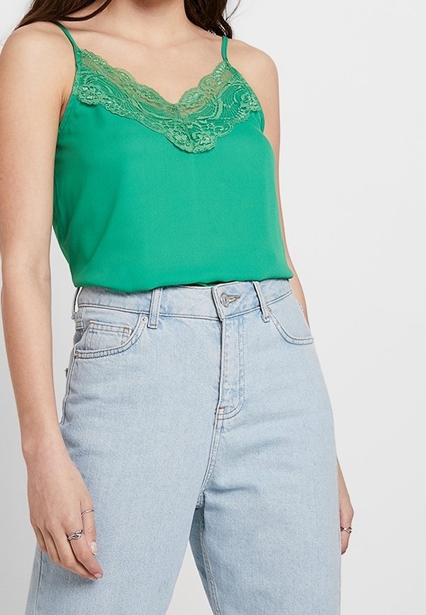 Camisole en satin vert avec une délicate bordure en dentelle le long du décolleté ; associée à un jean bleu clair taille haute.