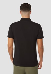 Zwarte polo met een korte kraag, korte mouwen en een rechte zoom. De stof lijkt glad met een klassieke pasvorm en minimale details.