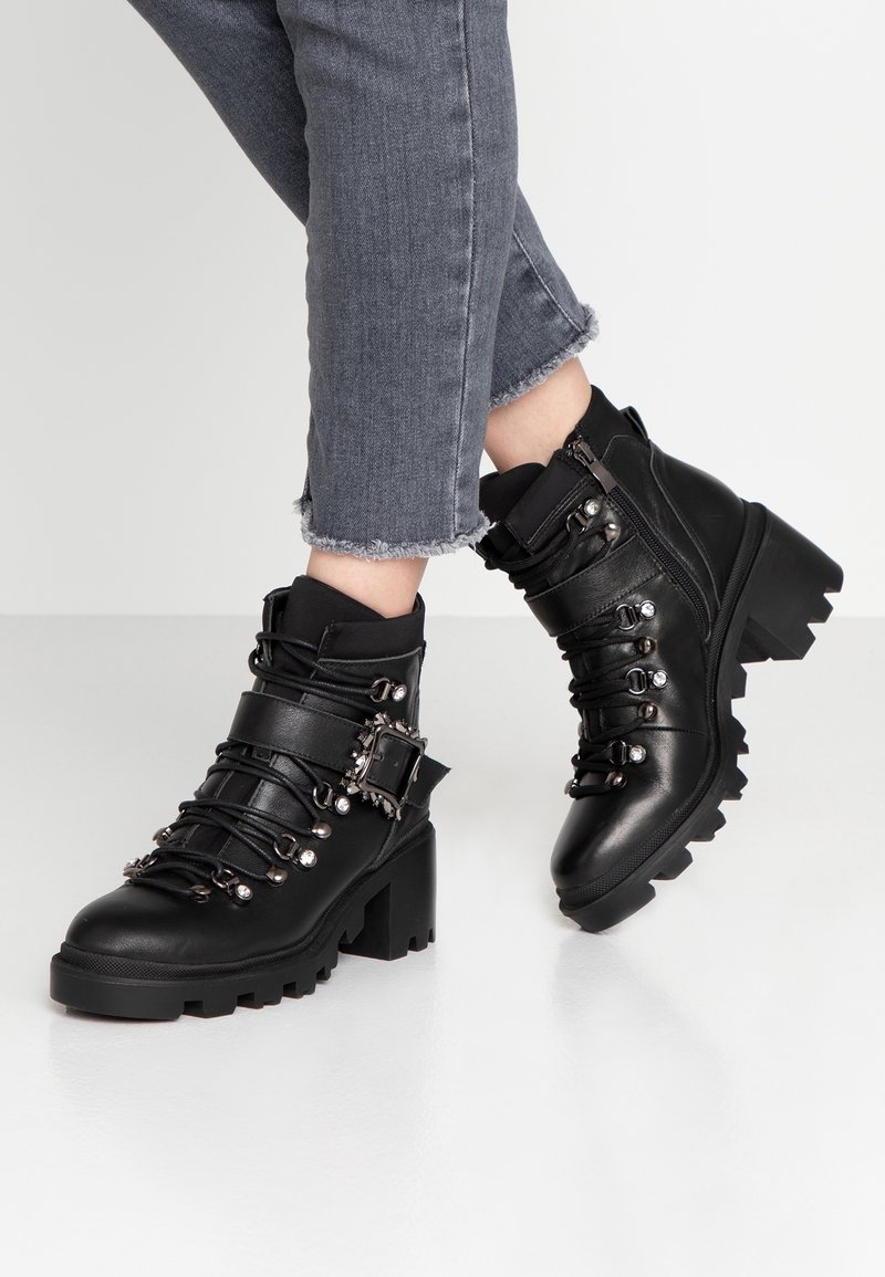 Stivali ankle neri in pelle con tacco grosso, caratterizzati da fibbie decorative, dettagli in metallo e design con lacci, dotati di suole testurizzate.