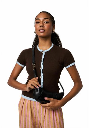 Ruskea ribbineulottu lyhythihainen neuletakki vaaleansinisin röyhelöin, yhdistettynä vaaleanpunaraidallisiin housuihin; pitää kädessään mustaa nahkaista pussilaukkua.