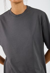 Dunkelgraues Baumwoll-T-Shirt mit rundem Halsausschnitt und kurzen Ärmeln, das eine glatte Textur und eine lockere Passform aufweist. Keine sichtbaren Muster oder Akzente.