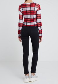 Suéter de punto a cuadros rojos y blancos con mangas largas, combinado con jeans ajustados negros y zapatillas plateadas. Diseño texturizado y ceñido.