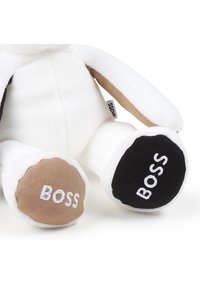 Pluszowa zabawka w białym kolorze z beżowo-czarnymi akcentami. Stopy ozdobione są kontrastowymi łatami z napisem "BOSS" w białym kolorze. Miękka tekstura na całej powierzchni.