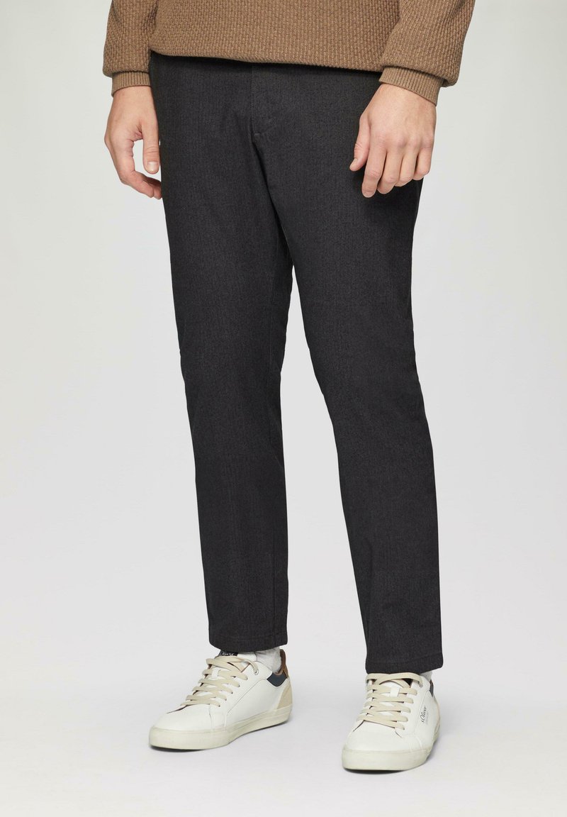 Donkergrijze, op maat gemaakte pants van gestructureerde stof, gecombineerd met witte en beige sneakers. De pasvorm is slank en gestroomlijnd.