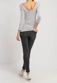 Chemise rayée grise et blanche avec un dos décolleté et des détails corail, assortie à un jean slim-fit foncé et des baskets blanches.
