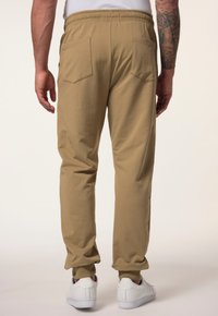 Beige Sweatpants mit lässigem Schnitt, ausgestattet mit elastischem Bund und Bündchen sowie zwei Gesäßtaschen, kombiniert mit weißen Sneakern.