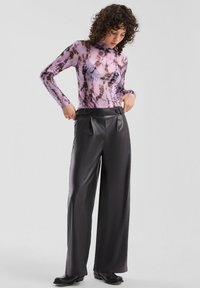 Doorzichtig topje met lange mouwen in paars met bruine patronen; gecombineerd met zwarte, wijde, hoge taille plooibroek van imitatieleder en zwarte laarzen met hak.