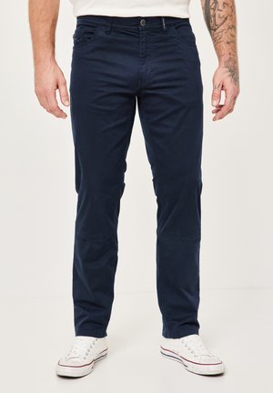 Navy blue chinos made of cotton with a smooth texture, featuring five pockets and a button closure. Worn with white sneakers.