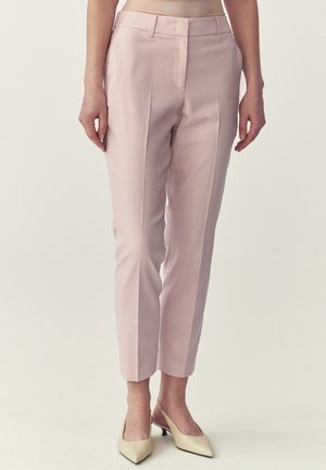 Donna che indossa pantaloni su misura rosa chiaro alla caviglia con piega frontale e scarpe slingback beige con tacco basso e punta a punta.