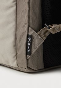 Gray fabric backpack corner with Columbia label; features textured surface, reinforced stitching, and breathable mesh paneling.