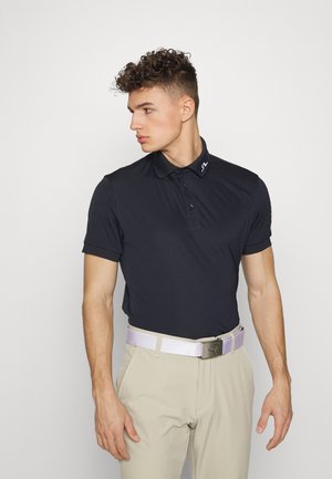 Marineblauw polo-shirt met een kraagontwerp en drie knopen, gecombineerd met beige broek en een lichtpaarse riem met een zilveren gesp.