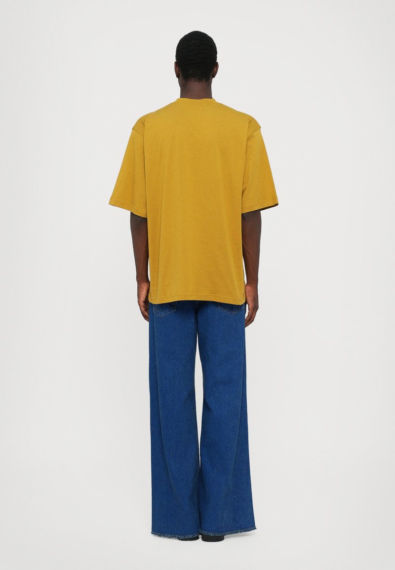 Yellow oversized t-shirt with short sleeves, paired with wide-leg blue denim jeans. The fabric appears soft with a relaxed fit.