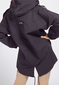 Czarna kurtka z kapturem o luźnym kroju, z elastycznymi mankietami i ściągaczem u dołu. Na plecach znajduje się subtelne logo. Gładka tekstura.